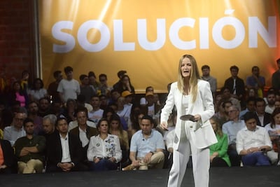 Soledad Núñez en traje blanco, hablando al público con expresión enérgica, fondo amarillo con la palabra 'SOLUCIÓN'.