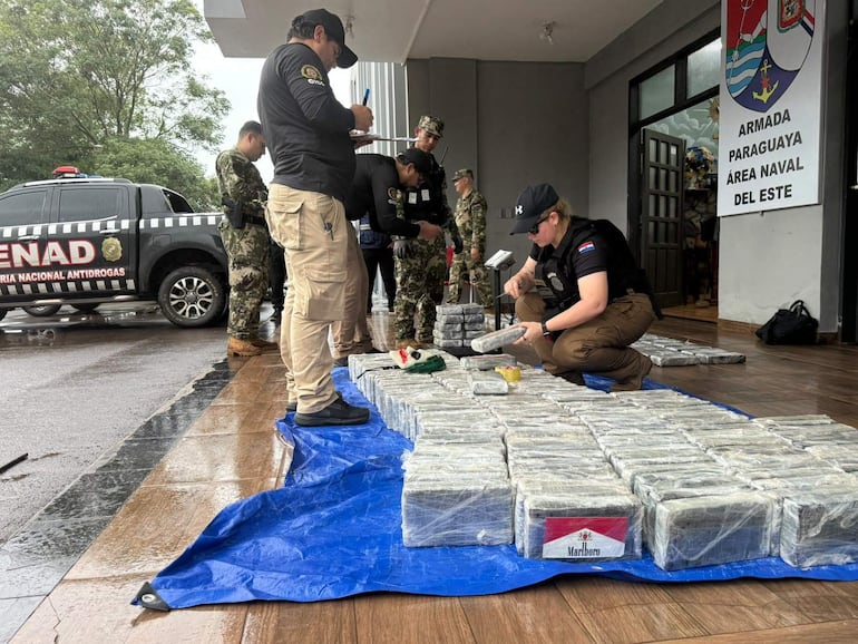 Agentes con uniformes de la SENAD registran paquetes de droga sobre una lona azul en un ambiente húmedo y oficial.