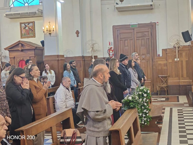 Enrique Kronawetter en misa, con expresión tranquila, rodeado de asistentes en un ambiente solemne y decoraciones religiosas.