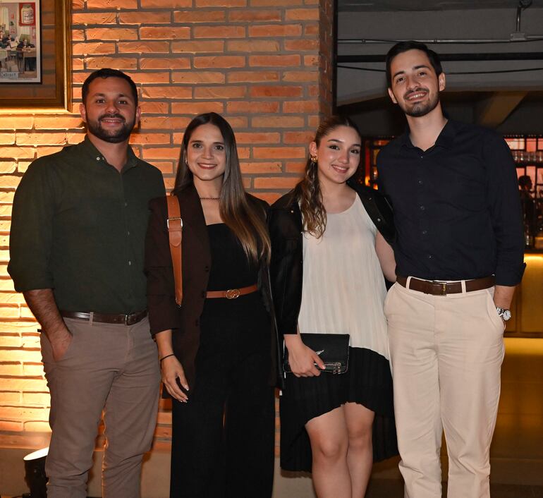 Grupo de cuatro personas felices posando: hombres con camisas oscuras y mujeres con blusas elegantes en un entorno acogedor.