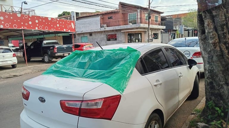 Vehículo blanco estacionado con lona verde mal colocada, en una calle urbana sin personas presentes.