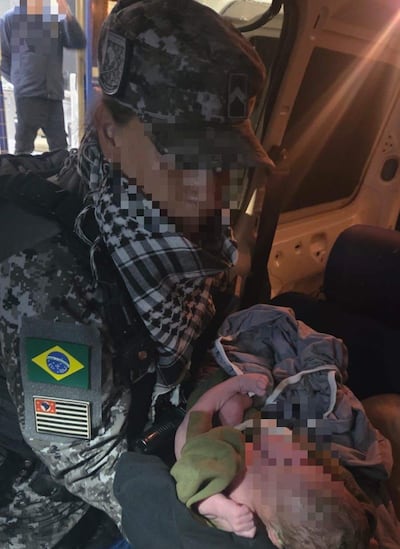 Militar brasileño serio sostiene a un recién nacido envuelto en ropa, dentro de un vehículo de asistencia.