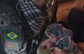 Militar brasileño serio sostiene a un recién nacido envuelto en ropa, dentro de un vehículo de asistencia.