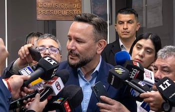Derlis León, con traje oscuro, responde preguntas de periodistas en un evento con cartel de 'COMISION DE PRESUPUESTO' al fondo.