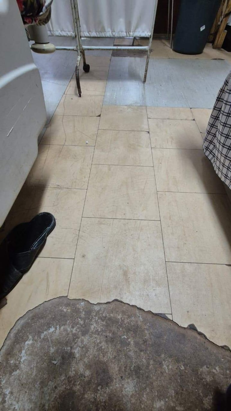 Suelo del Hospital Nacional de Itauguá con baldosas desgastadas y una zapatilla negra en el piso.