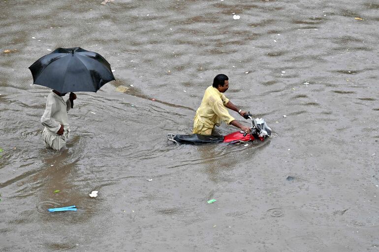 Un motociclista empuja su bicicleta por una calle inundada después de fuertes lluvias en Lahore.
