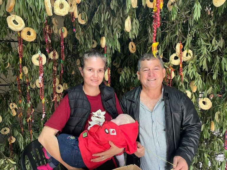 Mujer y hombre sonrientes junto a una niña, rodeados de hojas y decoraciones festivas en un ambiente cerrado.