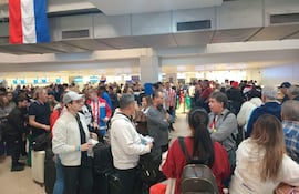 Multitud de aficionados con camisetas de Paraguay en fila en un aeropuerto, algunos sonrientes y otros conversando.