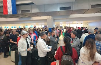 Multitud de aficionados con camisetas de Paraguay en fila en un aeropuerto, algunos sonrientes y otros conversando.