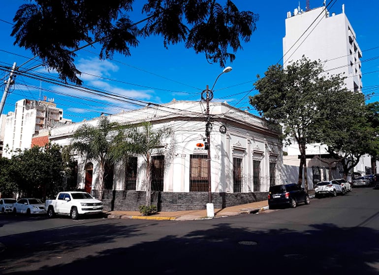 Calle urbana con edificio clásico a la izquierda y moderna construcción a la derecha, bajo un cielo despejado.