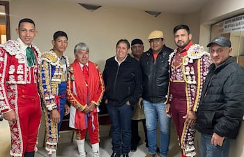 Seis toreros en trajes coloridos posan juntos; sonrisas visibles mientras observan a la cámara en un fondo neutro.