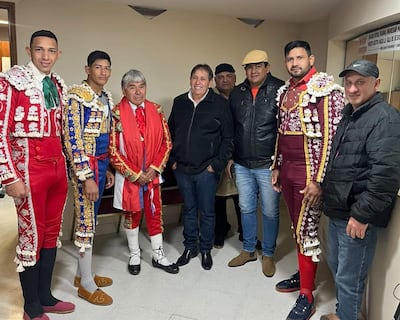 Seis toreros en trajes coloridos posan juntos; sonrisas visibles mientras observan a la cámara en un fondo neutro.