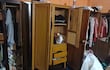 Interior desordenado de una habitación con tres roperos de madera abiertos y ropa esparcida por el suelo.