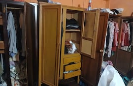 Interior desordenado de una habitación con tres roperos de madera abiertos y ropa esparcida por el suelo.