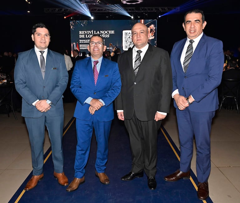 Cuatro hombres en trajes formales, sonriendo en la cena conmemorativa de la UIP, con una pantalla de fondo mostrando un mensaje celebratorio.