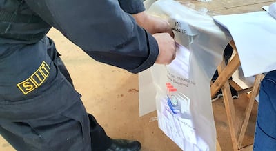 Miembro de seguridad con uniforme oscuro y insignia 'SIIT' manipula una urna electoral en un centro de votación.
