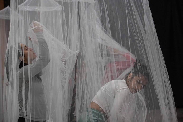 Dos mujeres con cabello oscuro manipulan telas blancas en un espacio artístico, concentradas y rodeadas de un ambiente creativo.