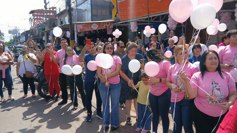 Grupo de 20 personas con camisetas rosas y globos, algunas mujeres posando para fotos, en un ambiente festivo al aire libre.