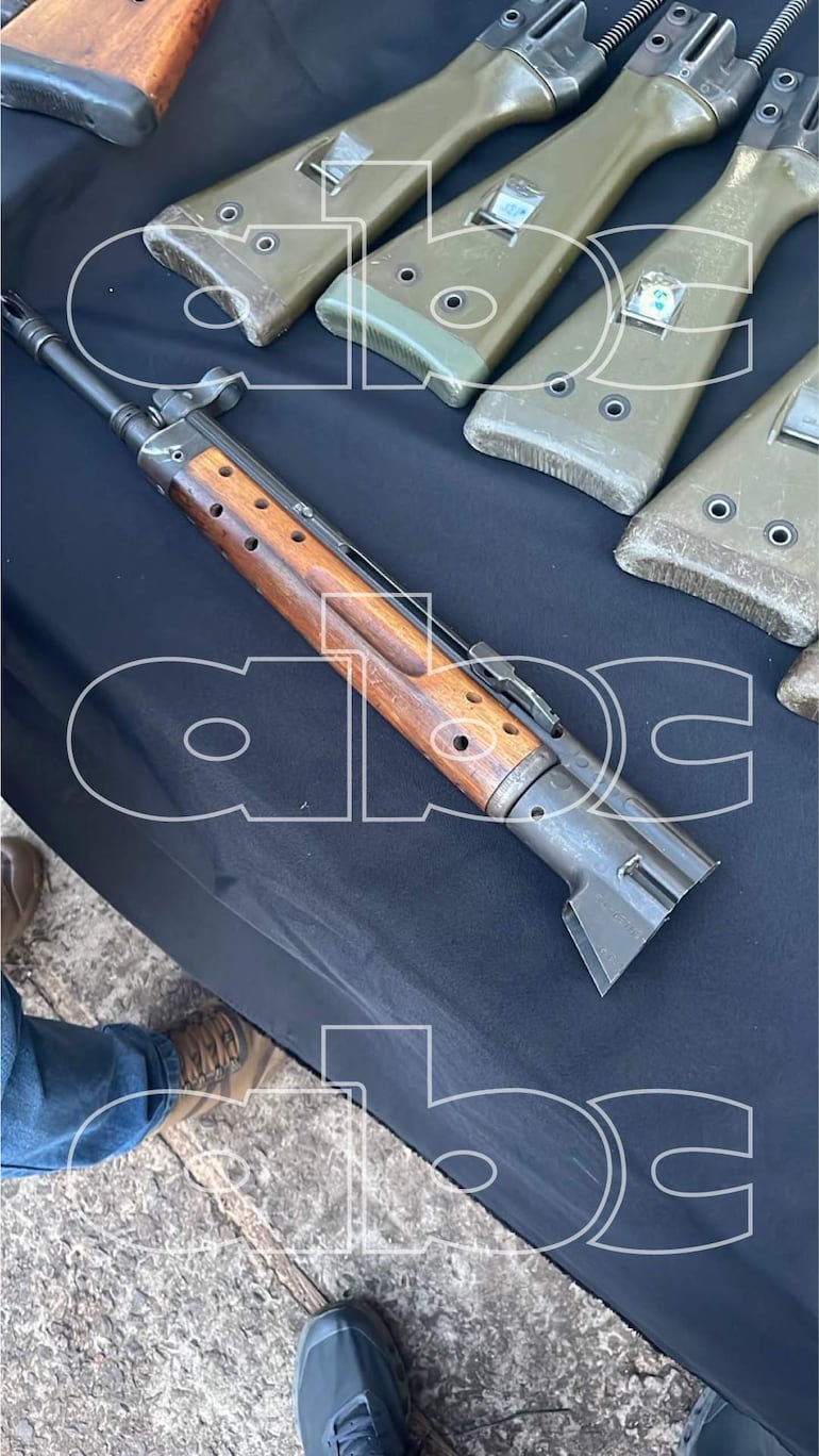 Un rifle con textura de madera sobre fondo negro, sin personas visibles en la imagen.