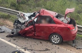 Automóvil rojo gravemente dañado tras accidente en ruta, con partes esparcidas y puerta abierta, en un entorno natural.