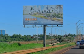 Cartel publicitario en carretera con paisaje de Encarnación y cielo despejado, llamando a descubrir la ciudad.