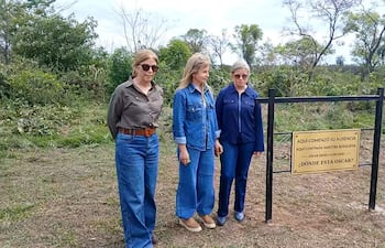 Tres mujeres en jeans y blusas conversan en un entorno natural, mientras sostienen un cartel sobre la desaparición de Oscar Denis.