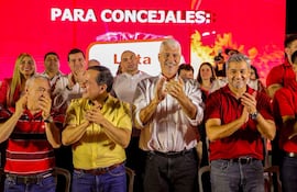 Arnoldo Wiens en camisa blanca aplaude en un acto político, rodeado de Arnaldo Samaniego y Mario Abdo Benítez, todos sonrientes.