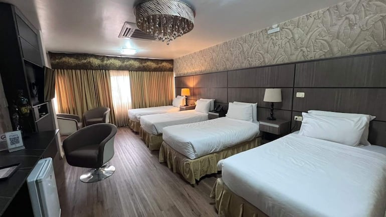 Habitación de hotel con tres camas individuales, decoración moderna y luz natural ingresando por ventana con cortinas amarillas.