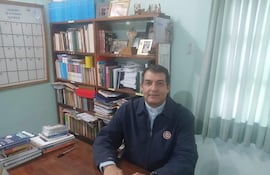 Monseñor Gabriel Escobar sentado en una oficina, con camisa blanca y chaqueta oscura, revisa un calendario en su escritorio.
