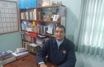 Monseñor Gabriel Escobar sentado en una oficina, con camisa blanca y chaqueta oscura, revisa un calendario en su escritorio.