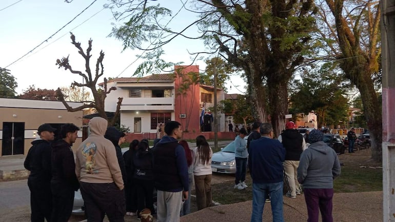 Grupo de personas de pie, vestidos en su mayoría con prendas oscuras, atentos frente a un edificio rojo durante la manifestación.