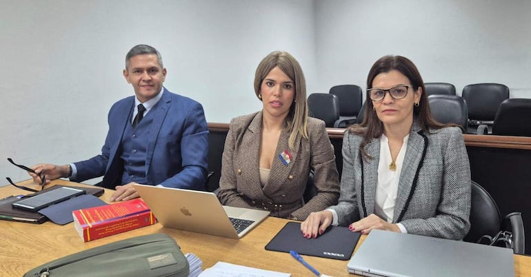 Hombre canoso con traje azul sostiene gafas, mujer en blazer se concentra, mujer de blusa blanca y abrigo negro usa gafas.
