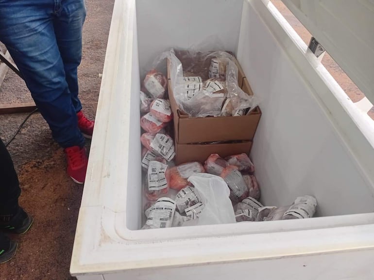 Cajas y paquetes de carne en un congelador, con las piernas de dos personas revisando productos.