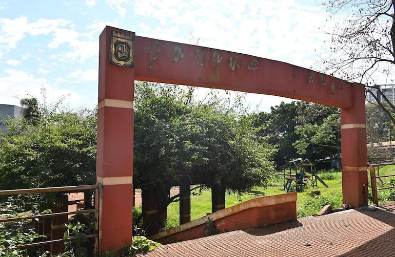 Entrada del Parque Verde con arco desgastado y vegetación densa, sin personas visibles.