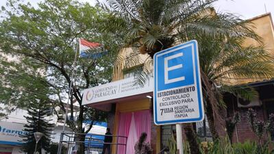 Edificio amarillo del Ministerio de Salud Pública y Bienestar Social con cartel de estacionamiento exclusivo, rodeado de árboles.