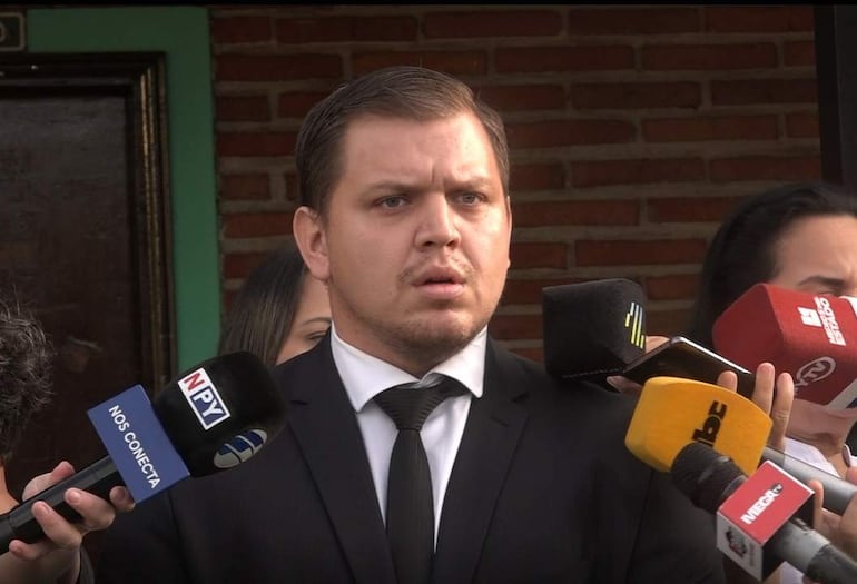 Rodrigo Delvalle en traje negro y corbata, rodeado de micrófonos y cámaras en un ambiente exterior formal.