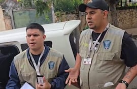 Dos hombres en chalecos beiges discuten en un ambiente urbano, mostrando identificaciones, mientras uno gesticula.