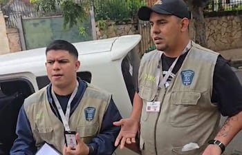 Dos hombres en chalecos beiges discuten en un ambiente urbano, mostrando identificaciones, mientras uno gesticula.