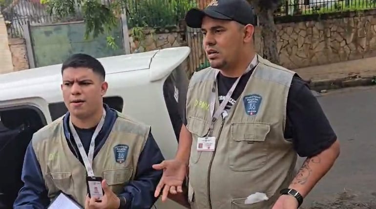 Dos hombres en chalecos beiges discuten en un ambiente urbano, mostrando identificaciones, mientras uno gesticula.