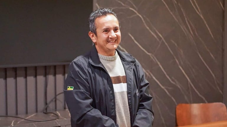 Hernán David Cubas sonriente, con abrigo negro y suéter claro, en ambiente interior con fondo de mármol.