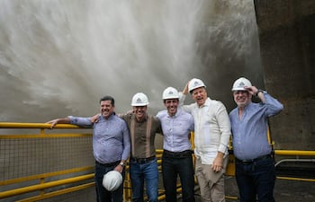 Cinco hombres con cascos de seguridad sonríen en un entorno industrial, con un gran chorro de agua de fondo.