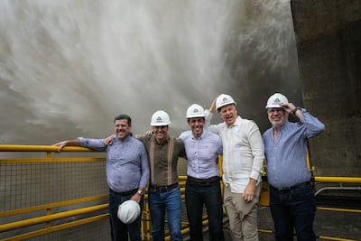 Cinco hombres con cascos de seguridad sonríen en un entorno industrial, con un gran chorro de agua de fondo.