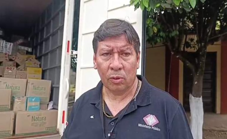Fiscal Miguel Quintana en camiseta negra del Ministerio Público, brindando declaraciones frente a un camión cargado con cajas.