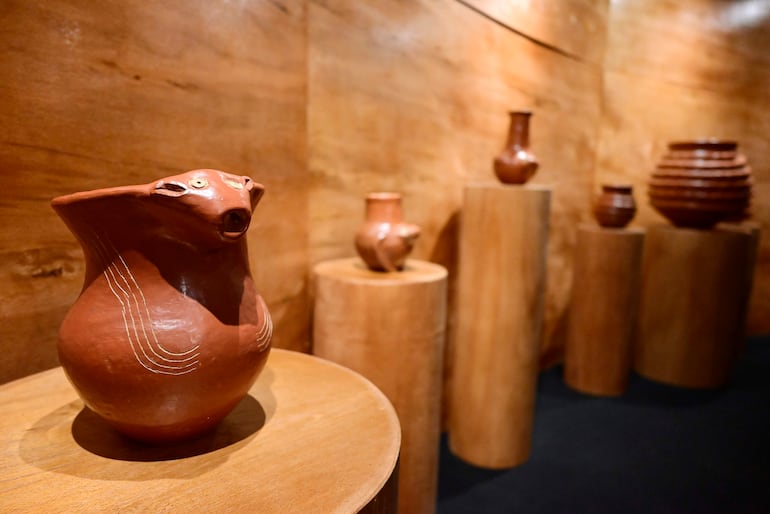 Urna en forma de cabeza de animal y otras piezas de cerámica sobre pedestales en un ambiente iluminado y acogedor.