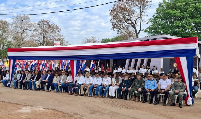 Asistentes con camisas blancas y sombreros en ceremonia al aire libre, rodeados de banderas rojas, blancas y azules.