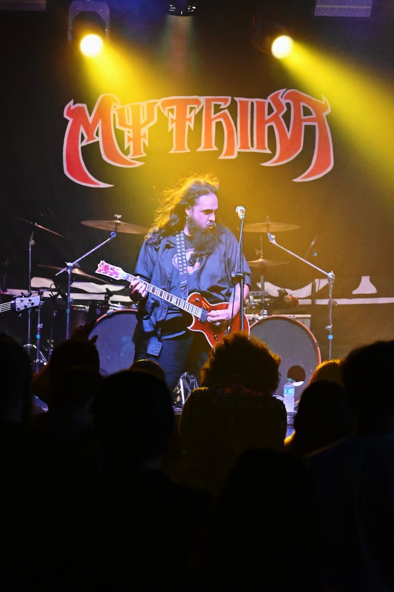 Julio Franco en el escenario, con camisa negra y guitarra eléctrica, rodeado de luces brillantes y un público animado.