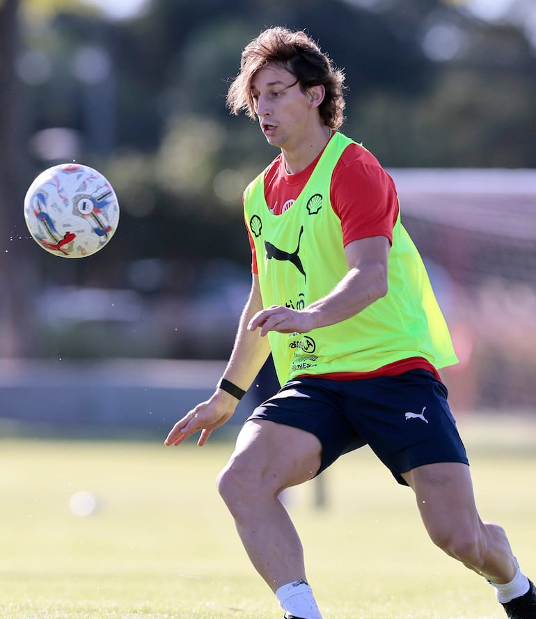 MATIAS GALARZA Futbolista en camiseta amarilla y roja, concentrado en recibir un balón, en un día soleado en el campo de entrenamiento.