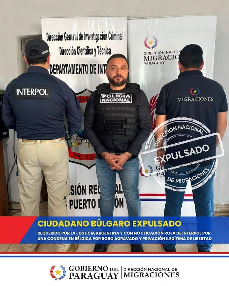 Tres funcionarios, uno con chaleco antibalas, formalizan la expulsión de un hombre en uniforme de INTERPOL en oficina gubernamental.