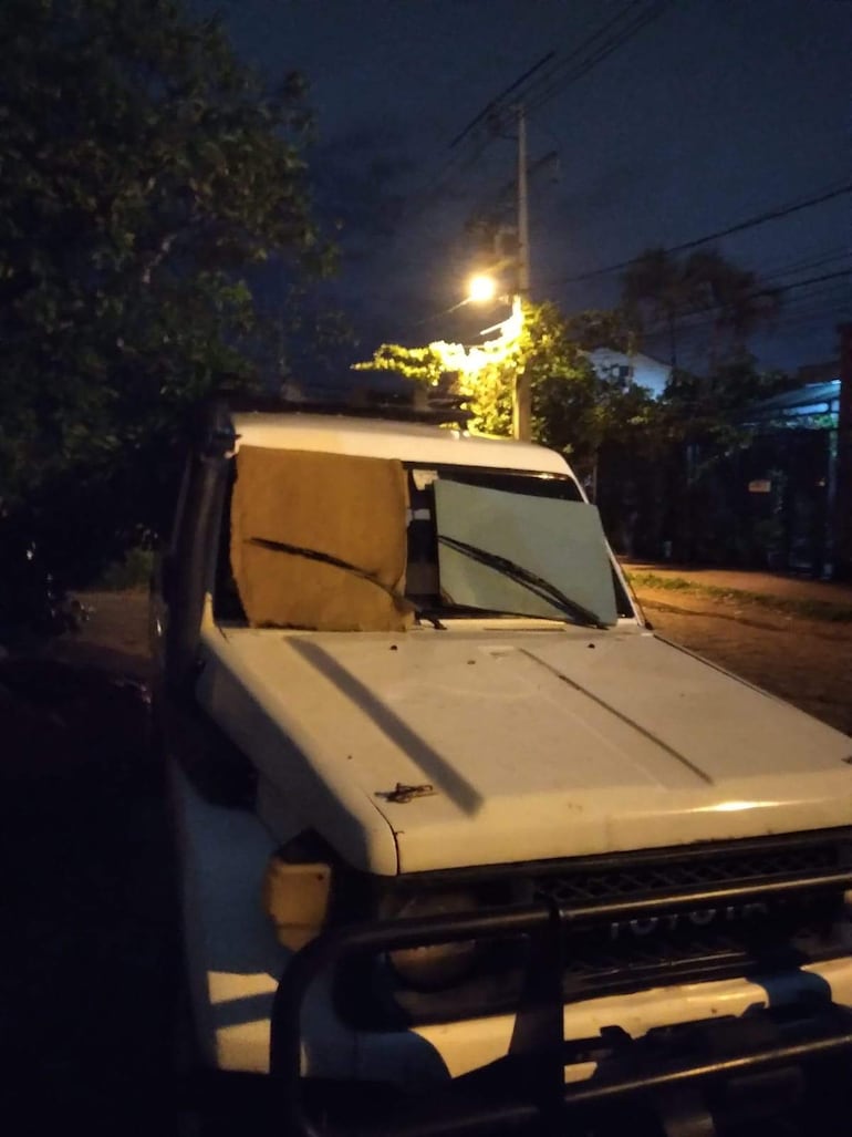 Camioneta blanca con almohadas en el parabrisas, aparcada en un área residencial durante el anochecer, sin personas visibles.