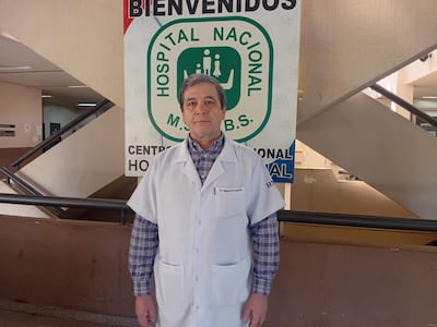 Dr. Miguel Ferreira, hombre de mediana edad con cabello canoso y bata blanca, en el Hospital Nacional de Itauguá con expresión seria.